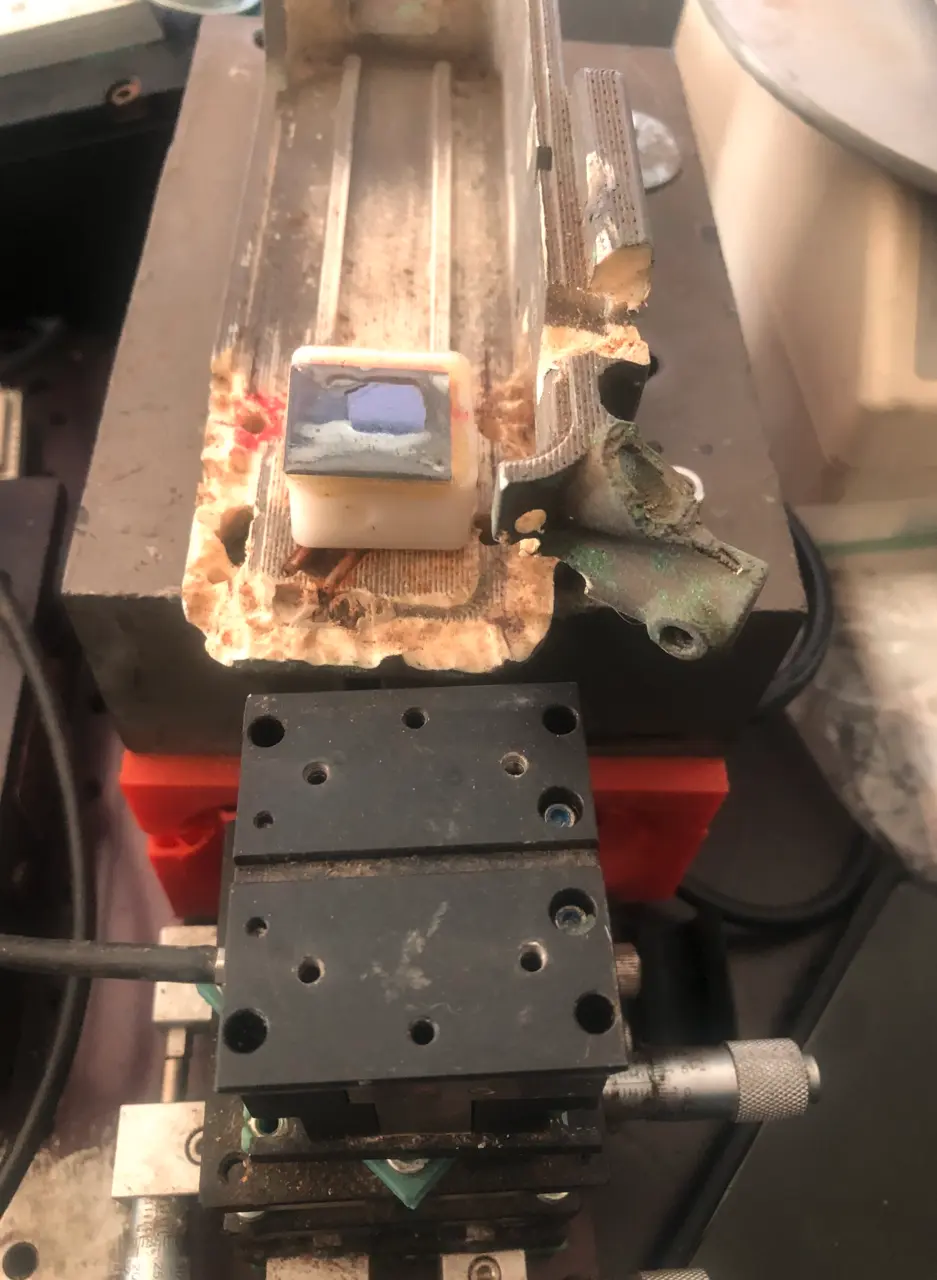 A chip epoxied at the tip of a rail above a black micropositioning stage with micrometer screws and a red 3D-printed part