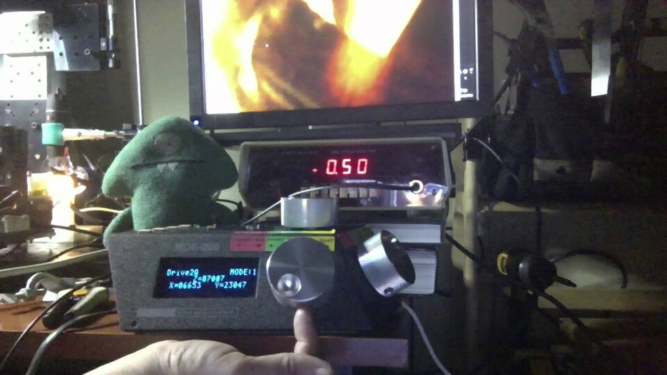 A lab bench: a positioner controller with a blue display, a benchtop meter reading -0.50 and a green felt figure with fangs